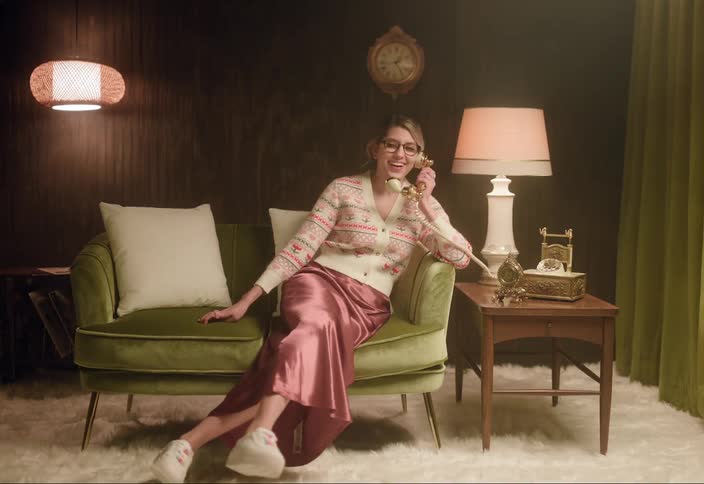 A woman sitting on a couch and picking up a phone to talk