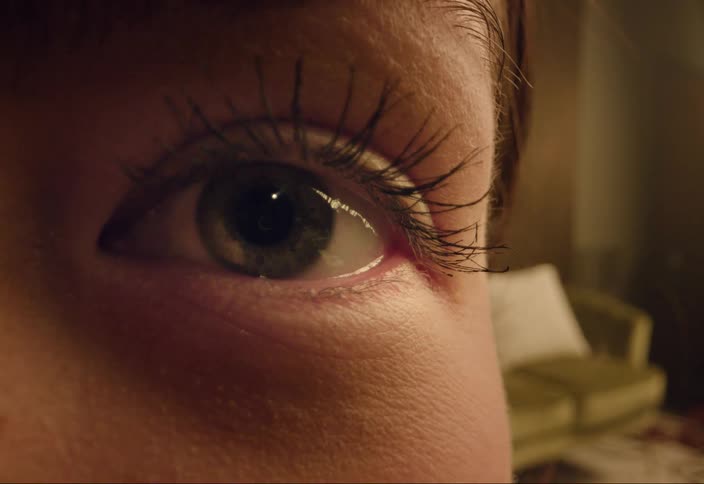 Closeup of womans eye with living room in background looking all around the room nervously sees something camera right and opens eyes in shock