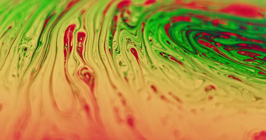 Green and red organic liquid is moving and mixing with yellow into variegated stripes as it stretches over the surface