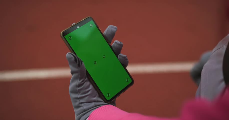 A woman wearing gloves is moving her finger across the green screen of her phone
