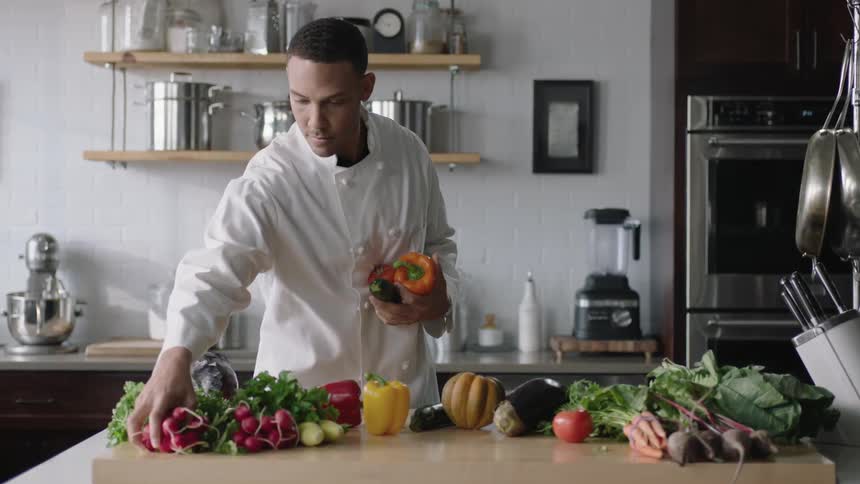 A chef chooses vegetables from a table before turning towards the kitchen sink