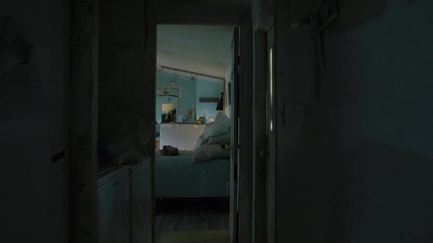 Man with beard white t shirt lies on bed with hands clasped together in bedroom praying