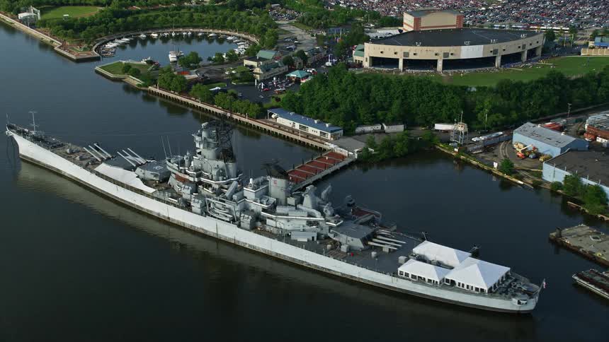 Aerial footage of military vessel USS New Jersey approaching Balzano Marine Terminal and BB&T Pavilion on Delaware River in Camden New Jersey during summer with boats docked nearby
