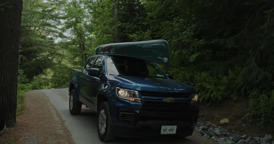 A truck with a canoe on top drives on the path