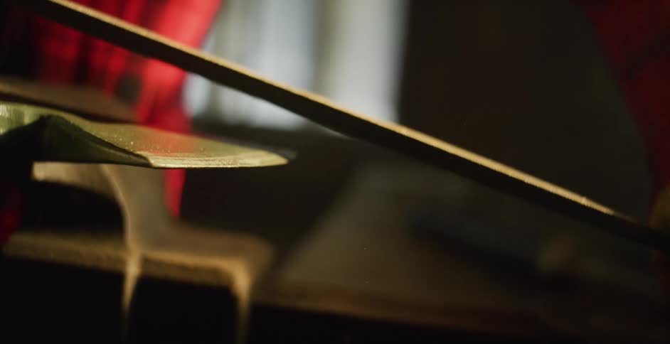 A man is using a file to sharpen the blade of an axe