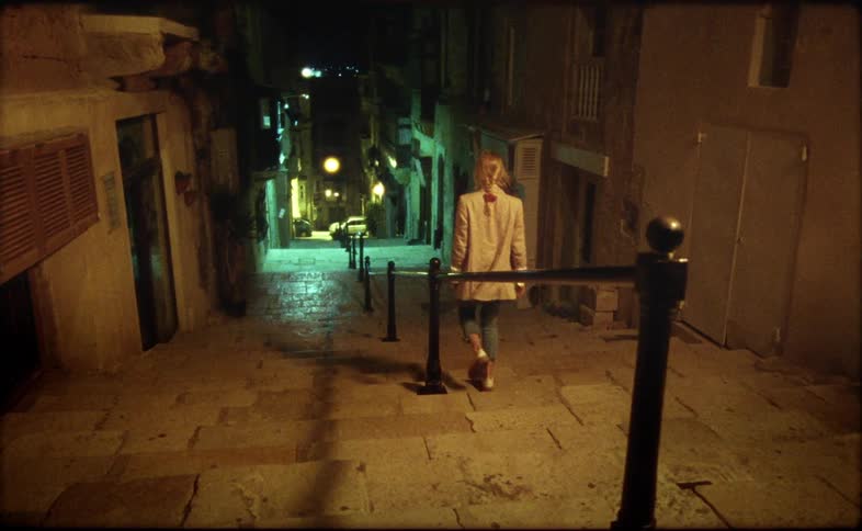 Woman walks down steps between apartment buildings at night