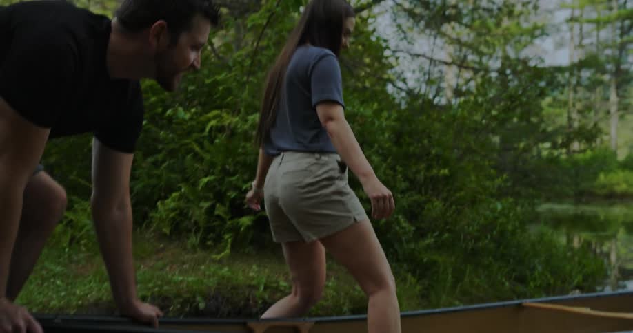 A man holds onto the back of a canoe while a woman carefully steps into it