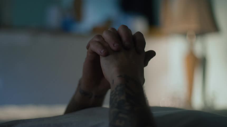 Man with his hand folded up and laying on the bed