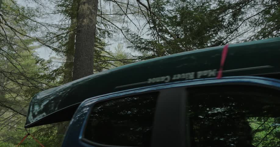 Car with canoe strapped to the roof driving through the forest
