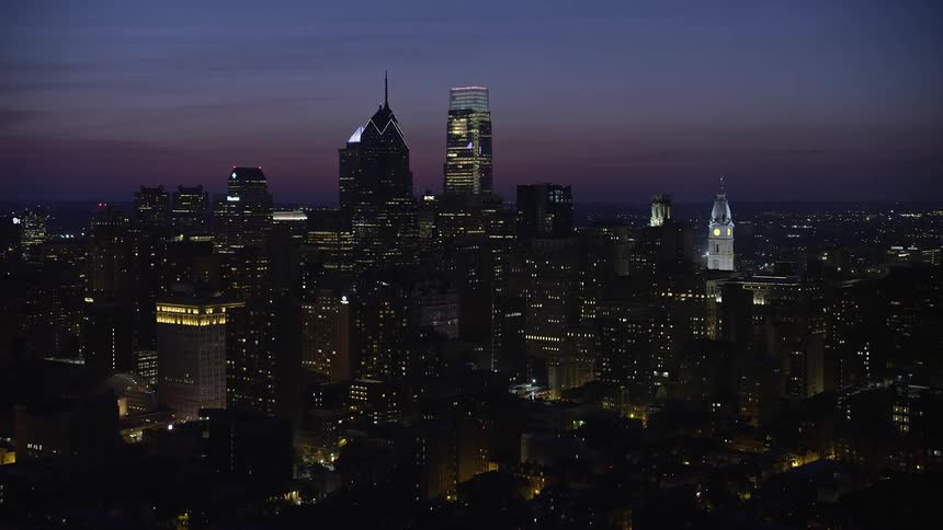 Aerial footage of skyscrapers in downtown Philadelphia including City Hall taken at night during partly cloudy conditions