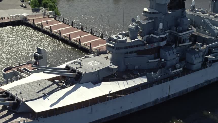 Aerial footage of battleship USS New Jersey gliding through the water during a sunny day in Camden NJ
