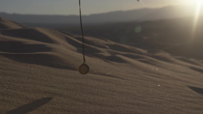 A person swings a necklace over the sand