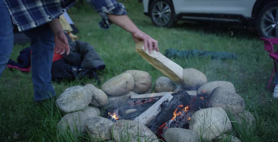 Father placing logs in rock fire pit on grassy lawn as daughter watches