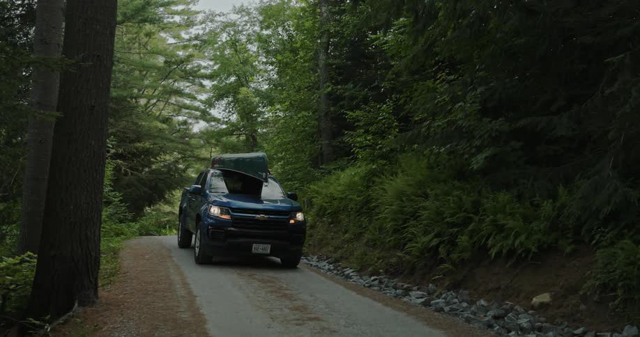 A truck with a canoe on the roof travels on a forest road