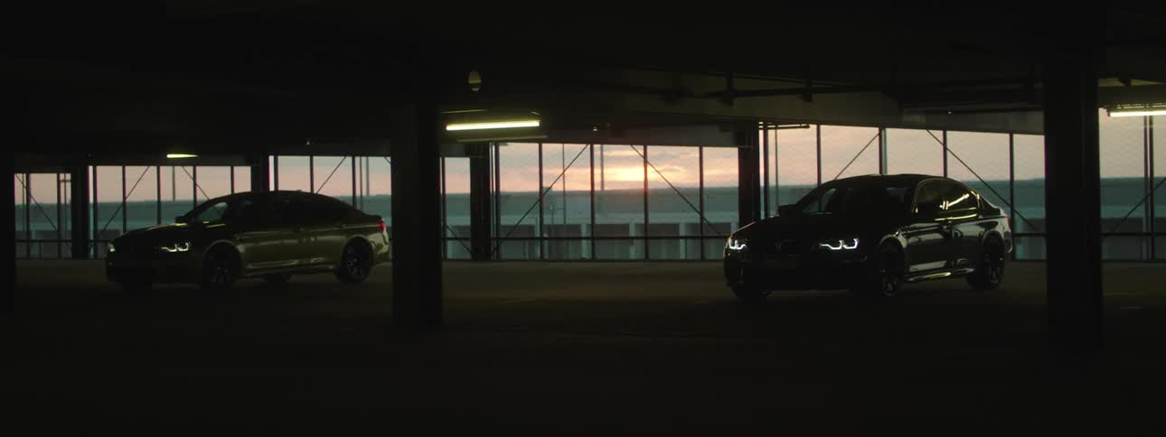 Sun sitting in red tinted sky is visible through glass behind two cars parked in garage