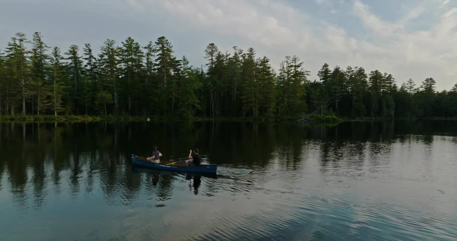 A man and woman paddle a boat across a lake together during the day