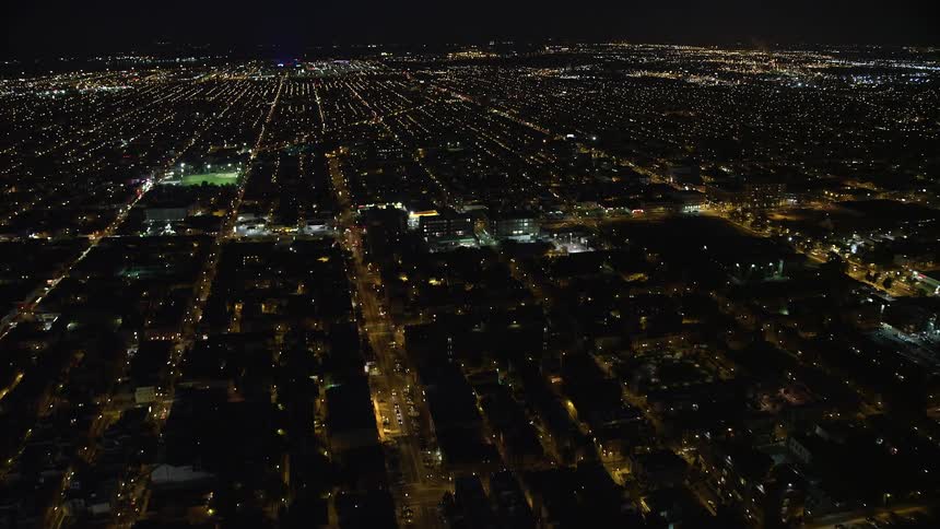 Lit tennis court and baseball field sit near each other in city stretching to the horizon at night