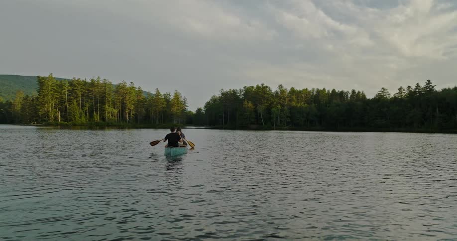 Man and woman paddle blue canoe through water between forest covered shores
