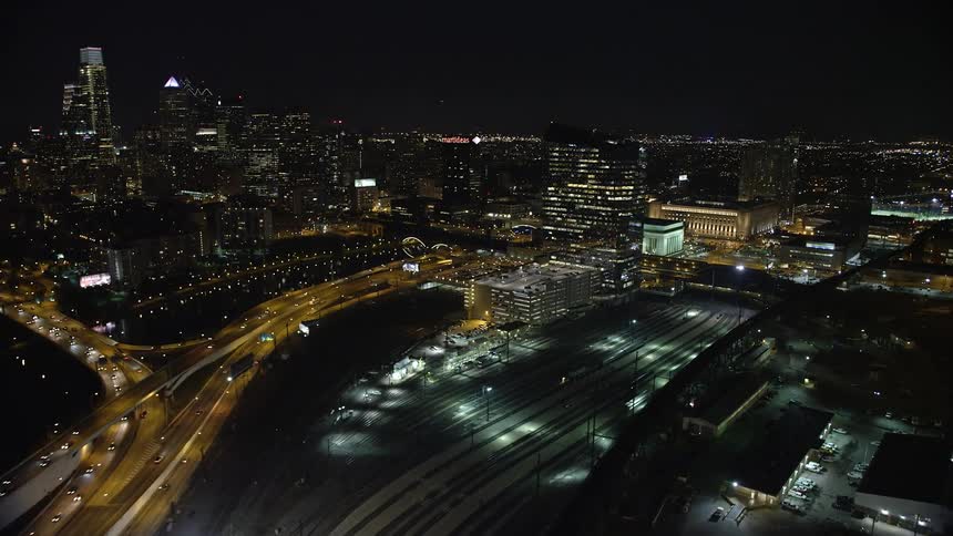 An aerial view at night of Philadelphias skyline with orbit bridges over the Schuylkill River Interstate 76 and a train yard revealing the citys downtown area