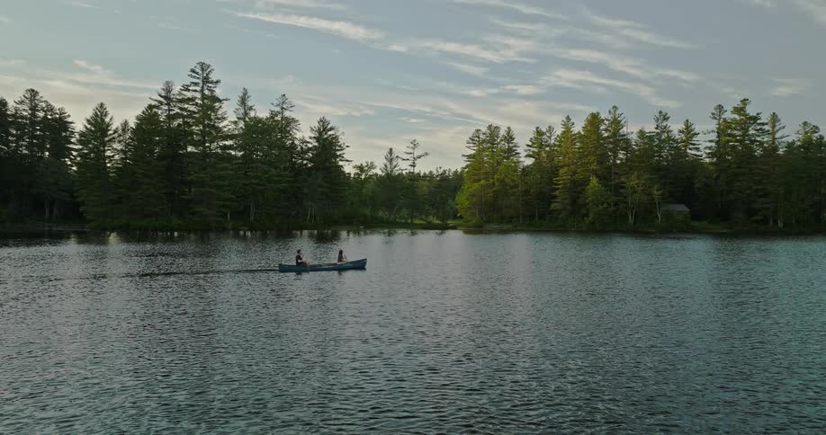 A man and a woman are rowing a canoe across a river surrounded by forests