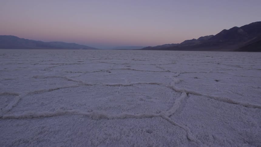 A large field is white with mountains in the distance