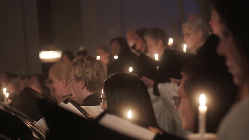 Congregation of people standing while looking at their books and holding candles