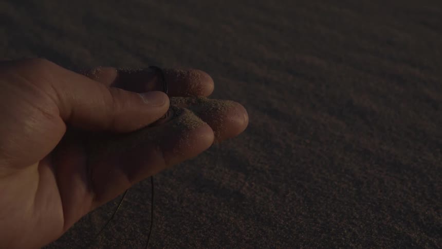 A hand holds a necklace covered in sand