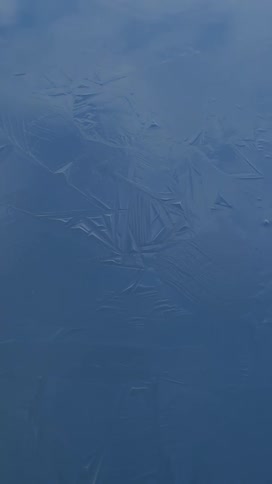 Textured thin ice floats on water as it reflect the clouds in the sky