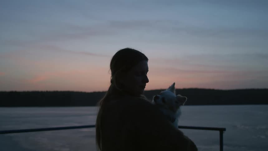A man holds his small dog while standing on a pier