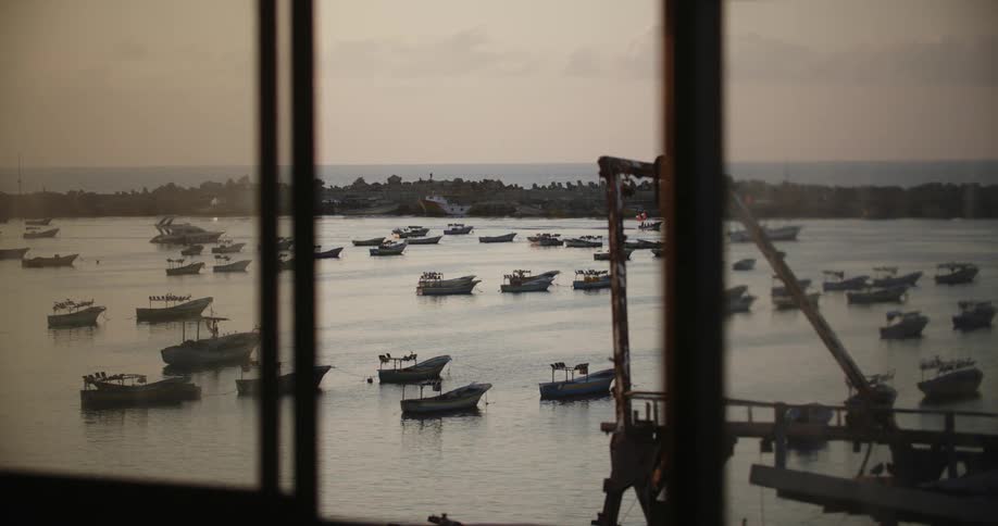 A small fishing boat heads into a harbor with a few people onboard and the ocean in the distance