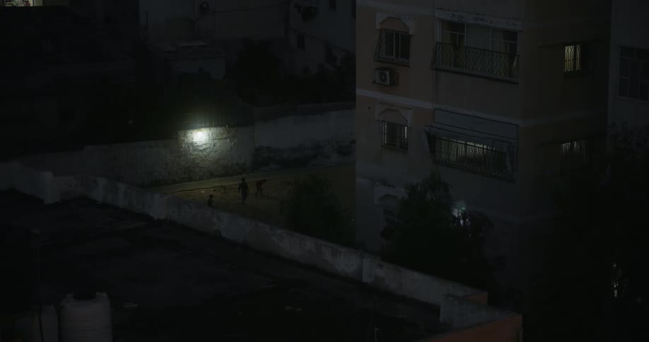 Three silhouettes of people in a courtyard near an apartment building