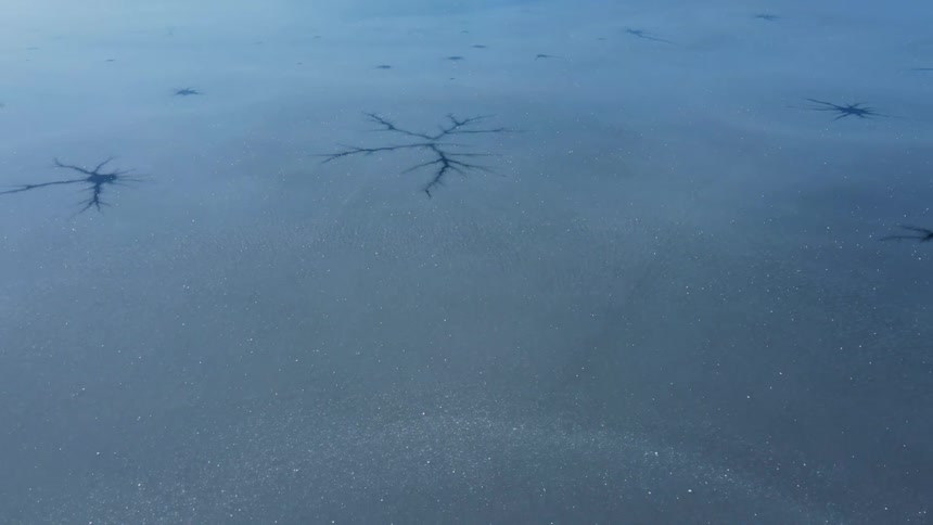Camera pulling back on full frame what appears to be a frozen lake with black inky veiny splotches frozen into it and glitter