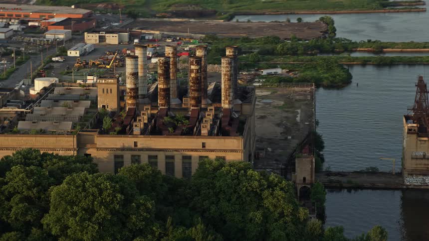 An abandoned manufacturing plant with multiple chimneys sits on the Delaware River waterfront during sunset in North Philadelphia PA