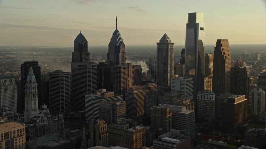 Stunning aerial footage of skyscrapers in Downtown Philadelphia during sunset showcasing the modern metropolis hazy skyline