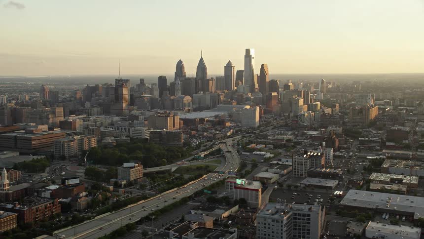 A stunning sunset view of Downtown Philadelphia skyline and the I-676 freeway with fast-moving traffic captured from an aerial view