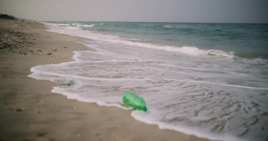 Discarded plastic bottles are lying on the beach as waves roll over the sand