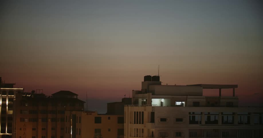 A large building that looks like a prison is shown at night and someone can be seen very far away walking outside of it