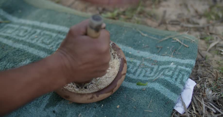 Person uses pestle to grind ingredients together on blanket set on ground