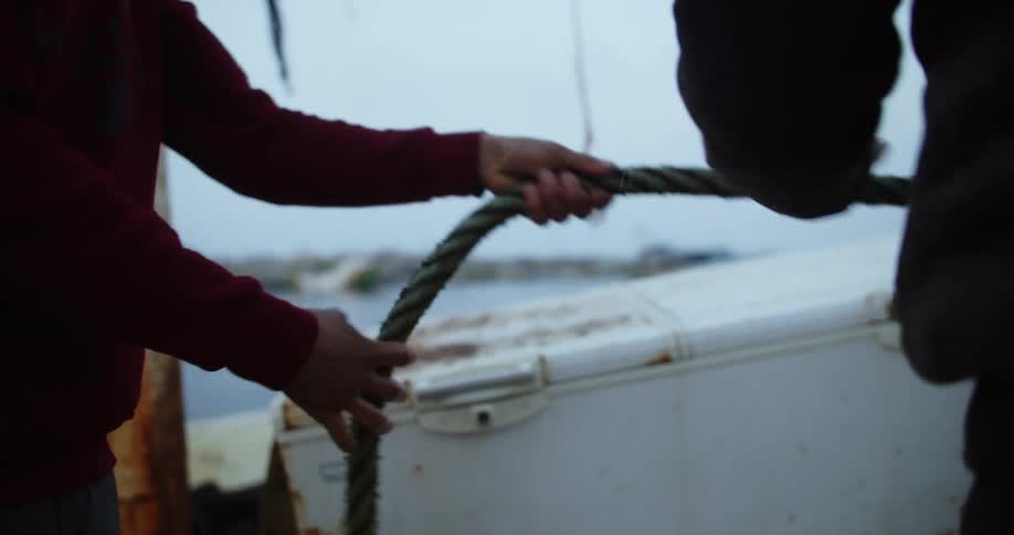 Two men on a boat are pulling on thick rope on a overcast day