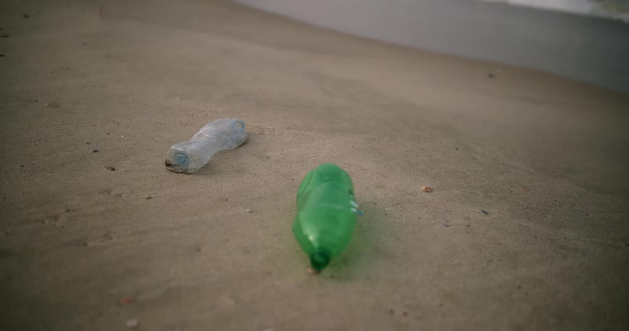 Discarded plastic bottles are lying on the beach as waves roll over the sand