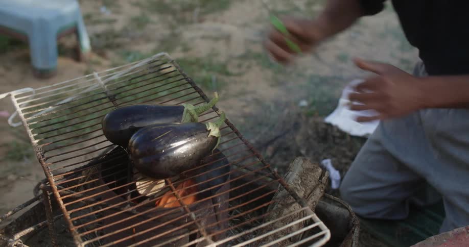 A man is grilling eggplants on the grill in the middle of the day time