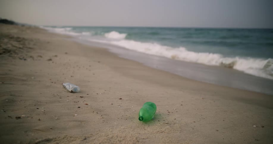 Discarded plastic bottles are lying on the beach as waves roll over the sand