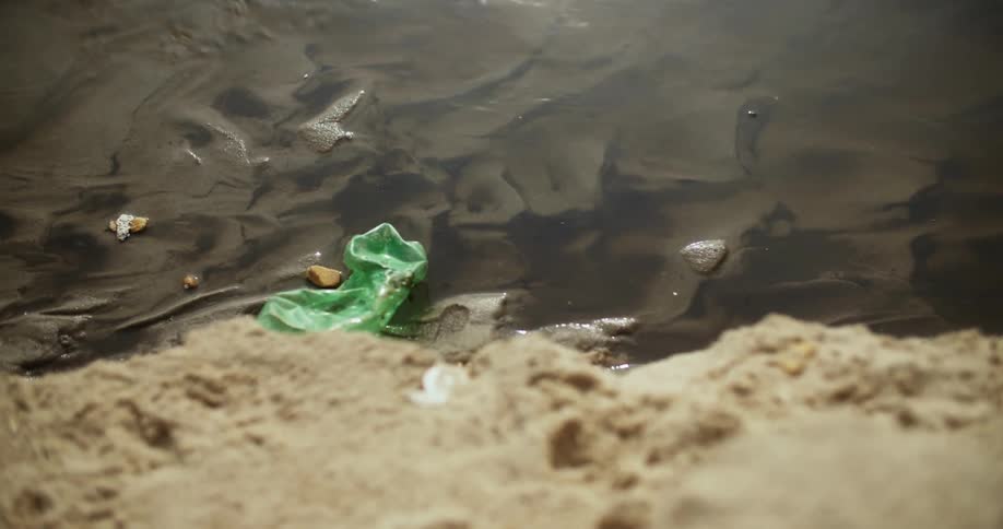 Close up of green plastic bottle littered on lake shoreline