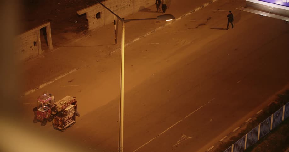 Merchants push street carts down side of busy road at night