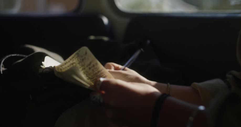 A person is writing on paper and sitting in a car