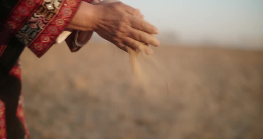 An adult is crushing a ball of dirt in their hands while standing in a barren field