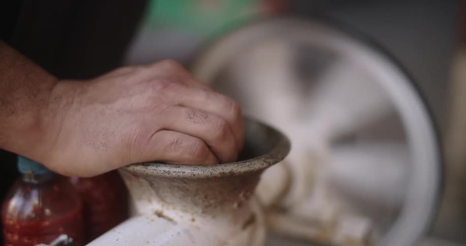A person uses a meat grinder with a wheel spinning in the background