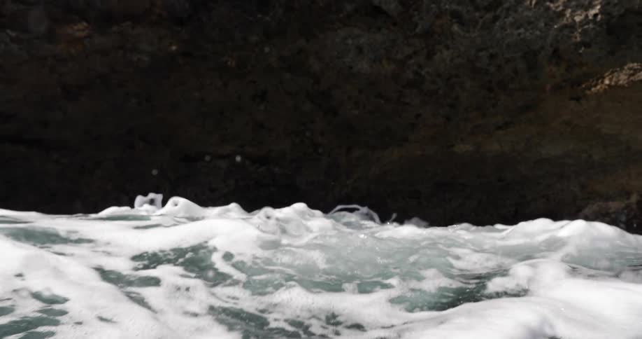 The sun shines on river water flowing out of a cave splashing and flying into the air
