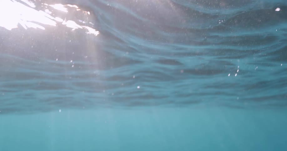 Rays of sunlight shine underwater as the water ripples and waves on the surface