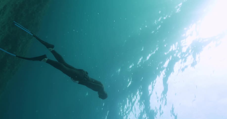 A man is swimming under water in a diving suit and slowly ascending to the surface in the daytime